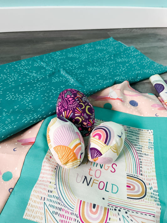 Vibrant and fun fabric eggs in a teal fabric nest on the floor.