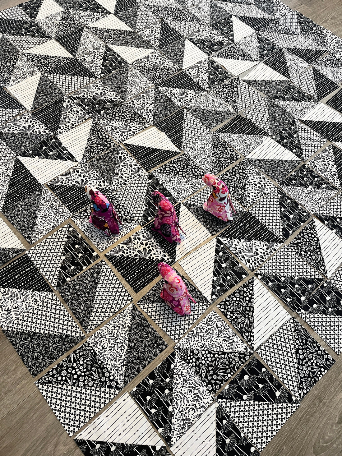 a black and white quilt laid out in a herringbone pattern with little stuffed animal toucans helping.