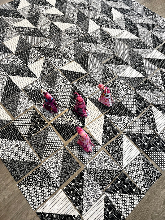 a black and white quilt laid out in a herringbone pattern with little stuffed animal toucans helping.